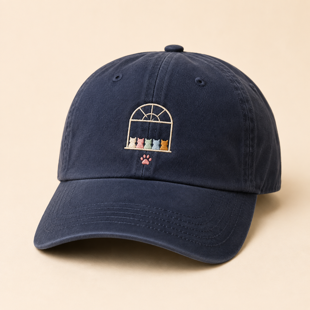 Washed navy dad hat embroidered with a small window, five colorful cat silhouettes and a pink paw